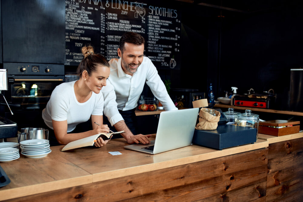 Happy small business owners working with laptop at cafe