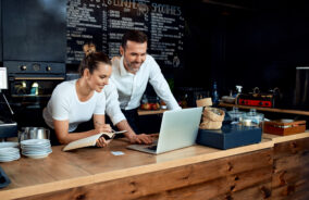 Happy small business owners working with laptop at cafe